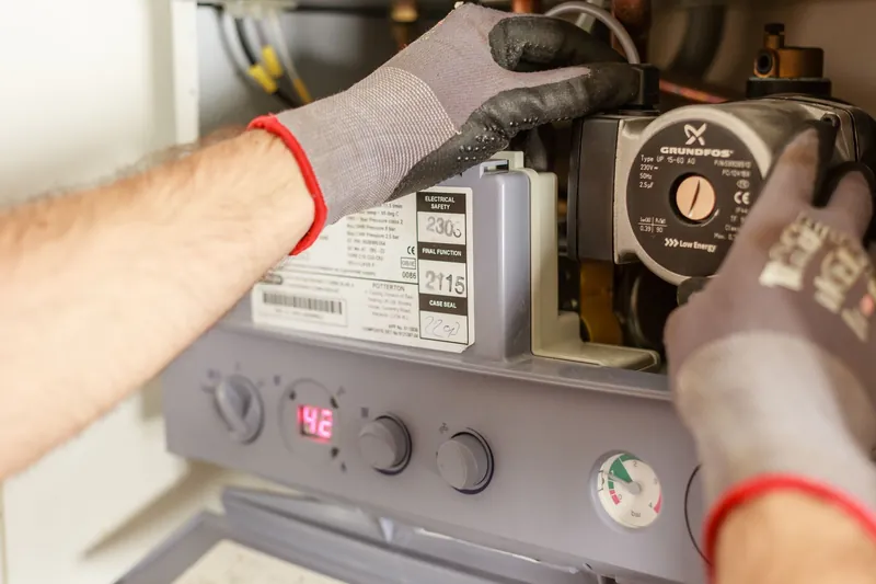 Plombier ajustant un chauffe-eau, gros plan sur les mains et les outils.