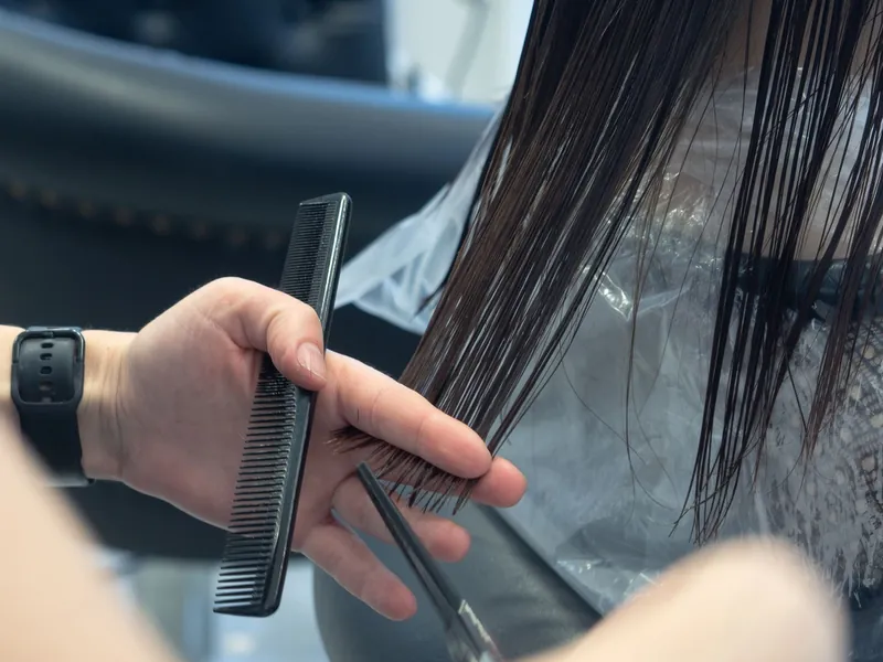 Coiffeuse coupant les pointes des cheveux d'une cliente en salon.